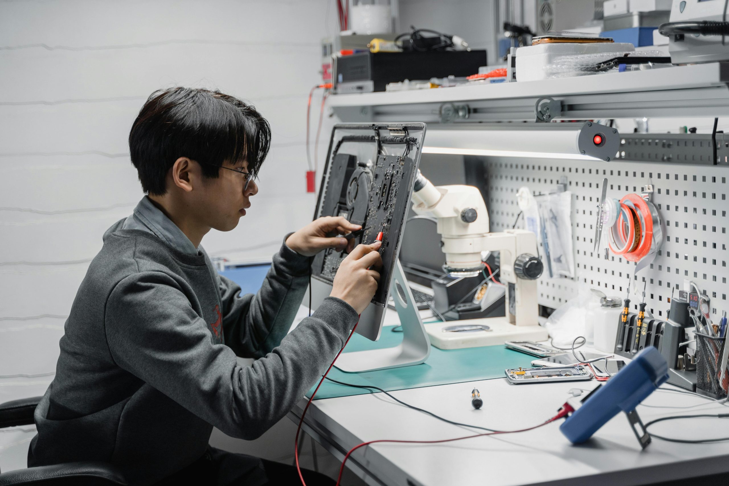 Focused young technician working on electronic repairs at a tech lab workspace.